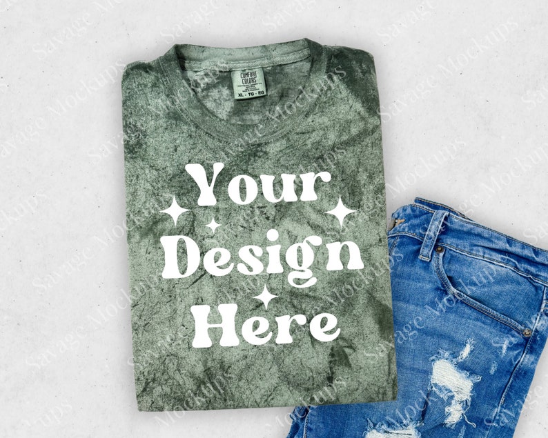 May include: A green tie-dye t-shirt with the text "Your Design Here" in white. The shirt is folded and laid on a white surface with a pair of blue jeans.