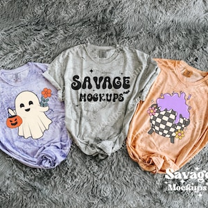 May include: Three t-shirts with Halloween-themed designs. One is lavender with a ghost holding a pumpkin and flowers. The second is gray with the text "SAVAGE MOCKUPS". The third is peach with a cauldron design.