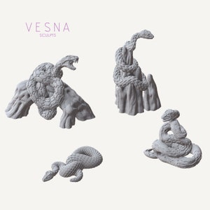 May include: Three 3D printed snake sculptures in various poses. One snake is coiled around a rock, another is on a rock formation, and the third is curled up on a flat surface.