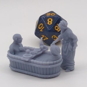 Könnte beinhalten: Eine Miniatur-Szene mit zwei Figuren, eine sitzt in einer Holzwanne mit einem Tisch und Essen, die andere steht daneben. Ein blauer und goldener 20-seitiger Würfel befindet sich im Hintergrund.
