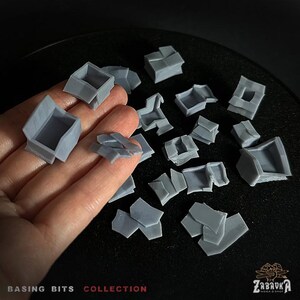 May include: A collection of gray plastic model building pieces for use in miniature wargaming or model railroading. The pieces are in various shapes and sizes, including walls, roofs, and other architectural details. The pieces are designed to be used as basing bits, which are small details that can be added to the base of a miniature to make it more visually appealing. The pieces are made of a durable plastic that can be painted and weathered to create a realistic look.