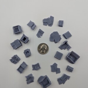 May include: A collection of 20 small, gray, plastic, 3D printed, miniature building pieces. The pieces are arranged in a circle on a white surface. A US quarter is in the center of the circle for scale.