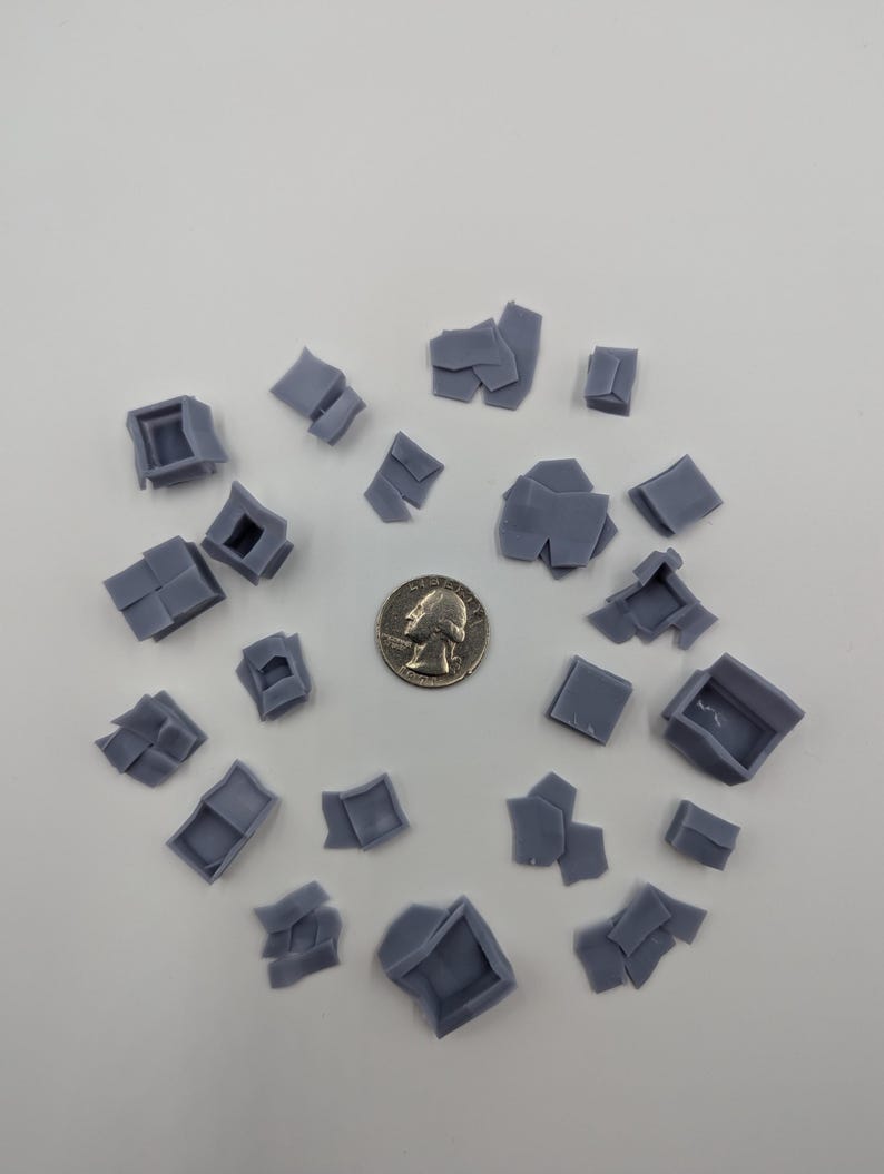 May include: A collection of 20 small, gray, plastic, 3D printed, miniature building pieces. The pieces are arranged in a circle on a white surface. A US quarter is in the center of the circle for scale.