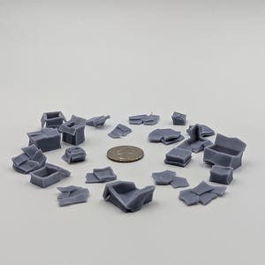 May include: A collection of gray, 3D printed, miniature cardboard boxes in various states of being crumpled and torn. The boxes are arranged in a circle on a white surface.