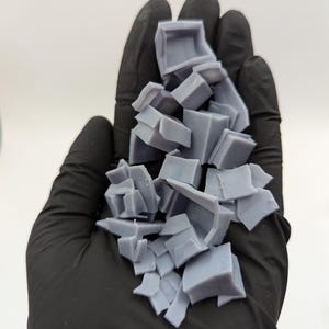 May include: A pile of broken gray plastic pieces, likely from a 3D printed model, held in a black gloved hand.