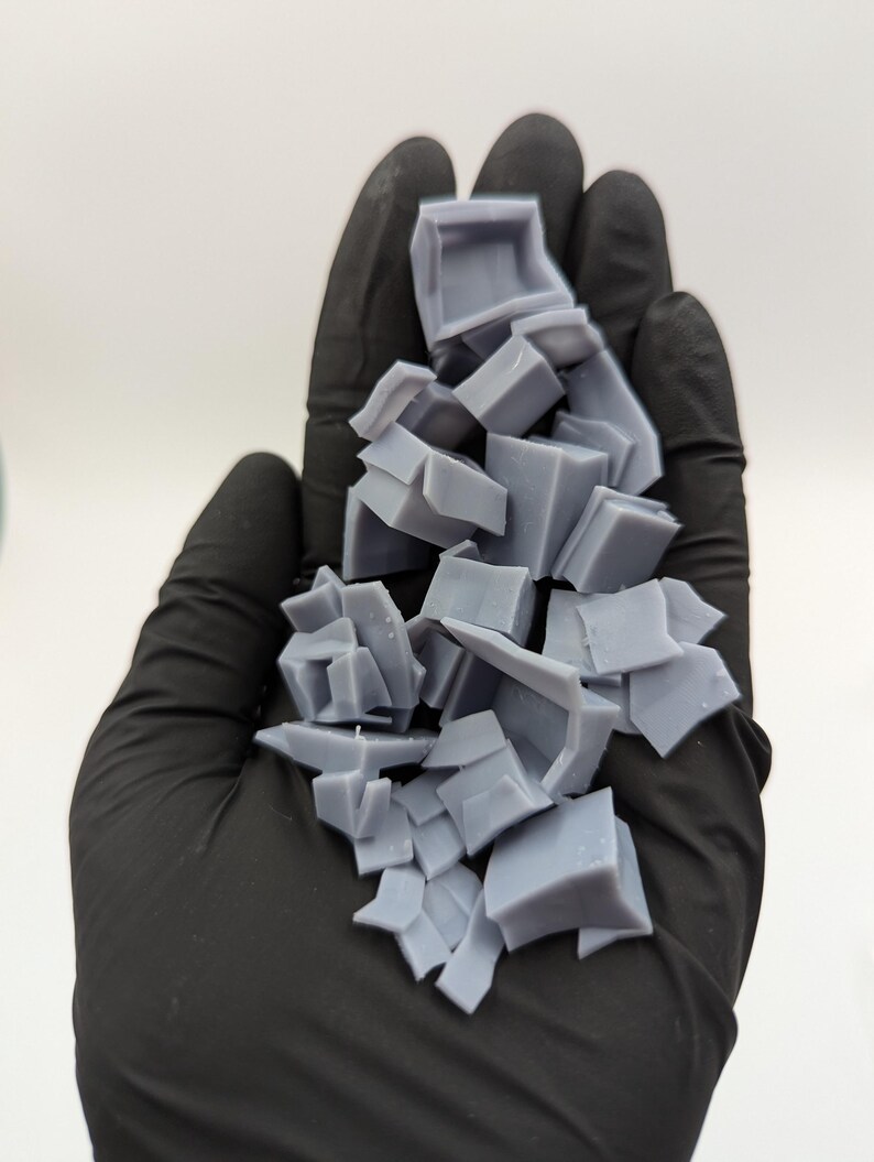 May include: A pile of broken gray plastic pieces, likely from a 3D printed model, held in a black gloved hand.