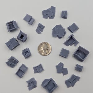 May include: A collection of 20 gray 3D printed plastic pieces, some are square, some are rectangular, and some are irregular shapes. The pieces are scattered on a white surface.