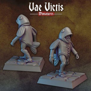 May include: Two gray painted miniature figurines of humanoid figures wearing fish costumes. The figures are standing on gray square bases with a textured surface. The text "Vae Victis - Miniatures" is printed on a brown background.