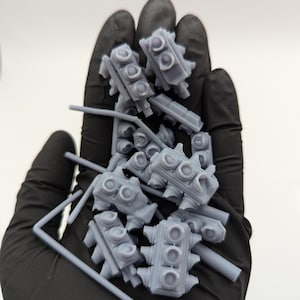 May include: A close-up of a hand holding a pile of gray plastic traffic light models. The models are small and detailed, with three lights each. They are perfect for use in model railroading or other miniature projects.