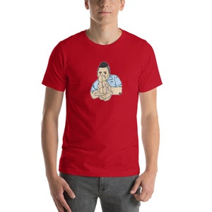 May include: A red short-sleeved t-shirt with a cartoon illustration of a person making a hand gesture. The person is wearing a light blue shirt.