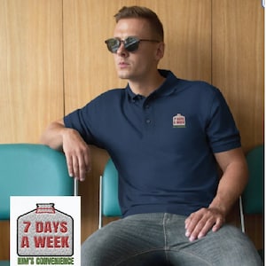 Pode incluir: Uma camisa polo azul marinho com um remendo bordado branco e verde que diz "7 Days A Week" e "Kim's Convenience".