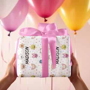 May include: A white gift box with a pink ribbon and a colorful cartoon animal print. The box is wrapped with a pink ribbon and the name "MADISON" is printed on the side.