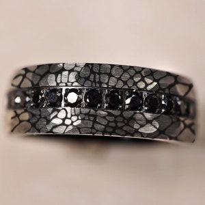 May include: A silver band with a textured, patterned surface and a row of black diamonds.