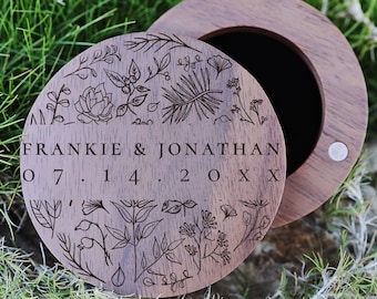 May include: A round wooden ring box with a floral design and the inscription "Frankie & Jonathan 07.14.20XX".