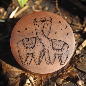 May include: A wooden box with a laser-engraved design of two llamas with hearts around them. The llamas are facing each other and appear to be kissing.