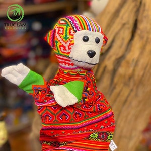 May include: A colourful monkey hand puppet with a red, green, yellow and blue patterned fabric. The puppet has a white face with black eyes and a black nose. The puppet is made of fabric and has a green arm.