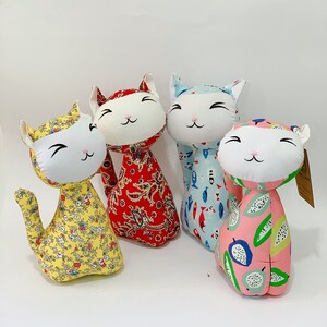 Può includere: Quattro giocattoli per gatti in tessuto fatti a mano. I gatti sono in piedi su una superficie bianca. I gatti sono tutti di colori e motivi diversi. Un gatto è rosso con un motivo paisley, uno è blu con un motivo a pesce, uno è giallo con un motivo floreale e uno è rosa con un motivo a frutta.
