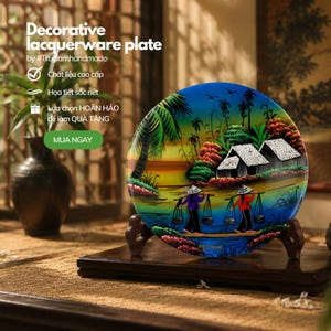 May include: A round decorative lacquerware plate featuring a vibrant landscape painting of two figures in conical hats carrying baskets on poles, with thatched-roof houses, palm trees, and a sunset gradient sky, displayed on a dark wooden stand.