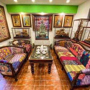 Puede incluir: Una sala de estar con una pared verde, un sofá, dos sillones y una mesa de café con un juego de tazas de té. Los muebles están cubiertos con tela de patchwork de colores. La habitación está decorada con obras de arte enmarcadas y esculturas de aspecto antiguo.