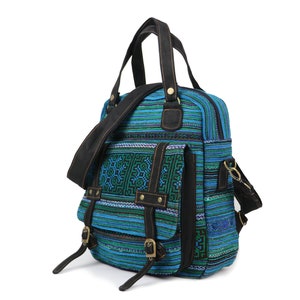 Op de afbeelding: Een blauwe en groene canvas rugzak met zwarte leren banden en accenten. De tas heeft meerdere vakken en een bovenste handvat.