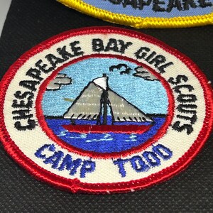 K&ouml;nnte beinhalten: Gestickter Aufn&auml;her mit einer nautischen Szene, die ein Segelboot auf blauem Wasser zeigt, mit dem Text "Chesapeake Bay Girl Scouts Camp Todd". Der Aufn&auml;her hat einen roten Rand und befindet sich auf schwarzem Hintergrund.
