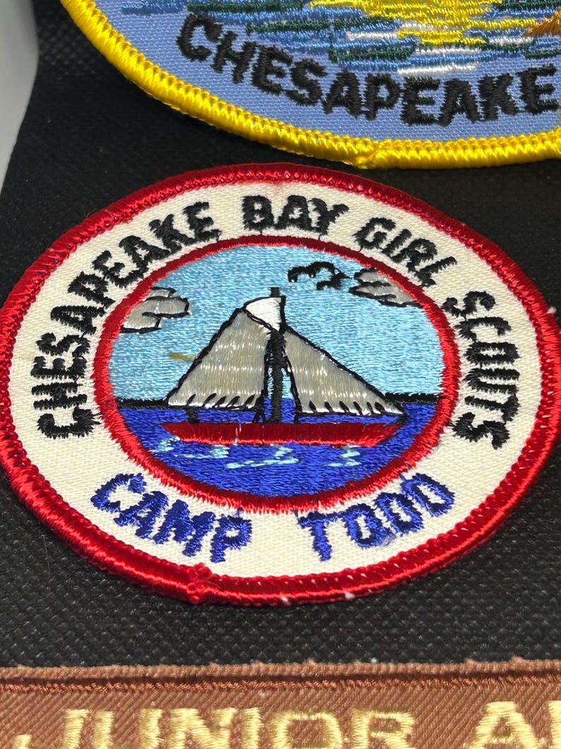 K&ouml;nnte beinhalten: Gestickter Aufn&auml;her mit einer nautischen Szene, die ein Segelboot auf blauem Wasser zeigt, mit dem Text "Chesapeake Bay Girl Scouts Camp Todd". Der Aufn&auml;her hat einen roten Rand und befindet sich auf schwarzem Hintergrund.