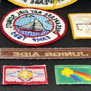K&ouml;nnte beinhalten: Eine Sammlung gestickter Aufn&auml;her, darunter ein runder Aufn&auml;her mit einer Berg- und Segelbootszene und ein rechteckiger Aufn&auml;her mit einem Regenbogen-Design. Die Aufn&auml;her weisen verschiedene Farben und Designs auf, wobei auf einigen Text sichtbar ist.