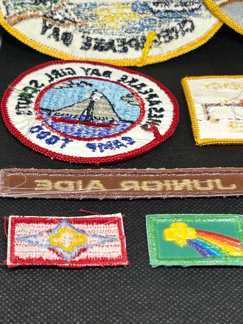 K&ouml;nnte beinhalten: Eine Sammlung gestickter Aufn&auml;her, darunter ein runder Aufn&auml;her mit einer Berg- und Segelbootszene und ein rechteckiger Aufn&auml;her mit einem Regenbogen-Design. Die Aufn&auml;her weisen verschiedene Farben und Designs auf, wobei auf einigen Text sichtbar ist.