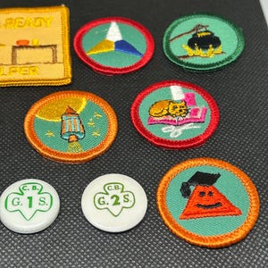 K&ouml;nnte beinhalten: Eine Sammlung farbenfroher gestickter Aufn&auml;her und Anstecknadeln. Die Aufn&auml;her zeigen verschiedene Designs, darunter eine Laterne, eine Katze und ein Dreieck mit einem Gesicht. Die Anstecknadeln sind wei&szlig; mit gr&uuml;nem Text. Die Aufn&auml;her haben rote und orangefarbene R&auml;nder.