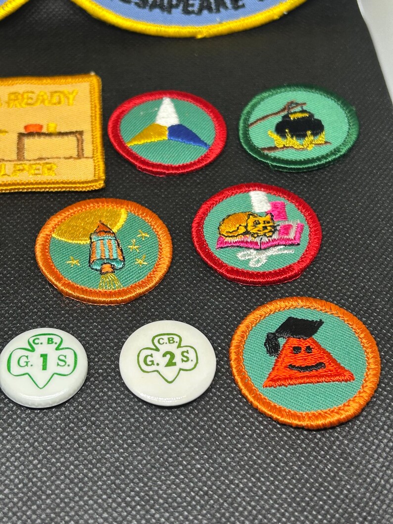 K&ouml;nnte beinhalten: Eine Sammlung farbenfroher gestickter Aufn&auml;her und Anstecknadeln. Die Aufn&auml;her zeigen verschiedene Designs, darunter eine Laterne, eine Katze und ein Dreieck mit einem Gesicht. Die Anstecknadeln sind wei&szlig; mit gr&uuml;nem Text. Die Aufn&auml;her haben rote und orangefarbene R&auml;nder.
