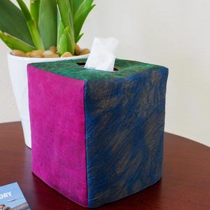 May include: A tissue box cover with a green, pink and blue design. The cover is made of wood and has a distressed finish.
