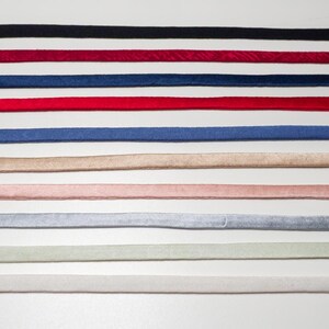 May include: A collection of ten thin velvet ribbons arranged in parallel horizontal rows. The colors include black, deep red, navy blue, bright red, royal blue, beige, light pink, light gray, pale green, and off-white, each with a soft texture.