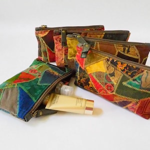 Op de afbeelding: Een set van vijf kleurrijke patchwork-ritszakjes met een gouden rits. De zakjes zijn gemaakt van verschillende stoffen en hebben een verscheidenheid aan patronen. Een klein wit flesje ligt voor de zakjes.