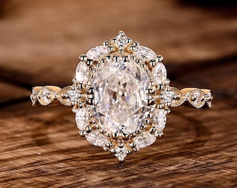 May include: A gold engagement ring featuring a large oval-cut diamond. The central stone is encircled by smaller diamonds in a halo setting. The ring's band has detailed embellishments.