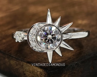 Op de afbeelding: Een zilveren ring met een grote, heldere, ronde edelsteen omringd door kleinere edelstenen. De ring heeft een zon- en maandesign met een puntige zon en een halve maan.