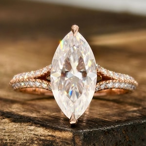 Op de afbeelding: Een verlovingsring met marquise-geslepen diamant en een roségouden band. De ring heeft een grote, heldere, marquise-vormige diamant als middelpunt, met kleinere diamanten langs de band. Op een houten oppervlak.