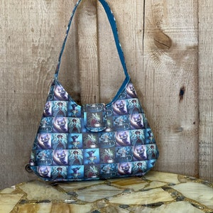 May include: A blue and white patterned tote bag with a shoulder strap. The bag features a repeating pattern of a cat, a rabbit, and a clock.