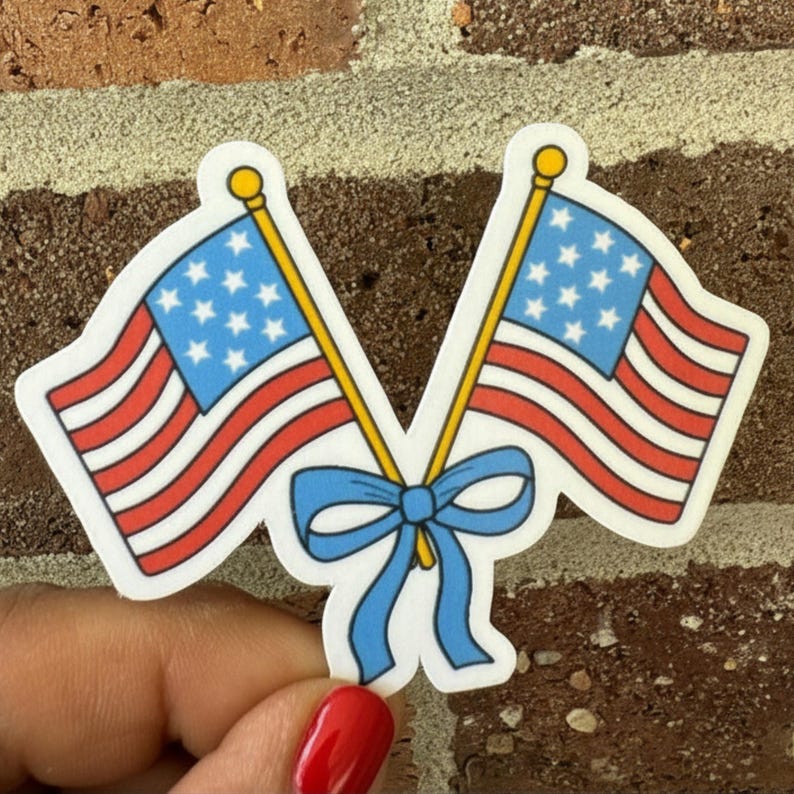 May include: A sticker featuring two American flags with red and white stripes and blue star fields. The flags are connected by a blue bow. The flags have yellow poles and are set against a brick background.