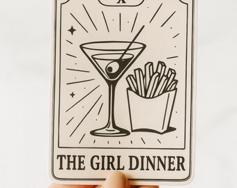 May include: A rectangular sticker with a black and white illustration of a martini glass with an olive, a side of fries, and the text "THE GIRL DINNER". The sticker has a tarot card design with the number "X" at the top.