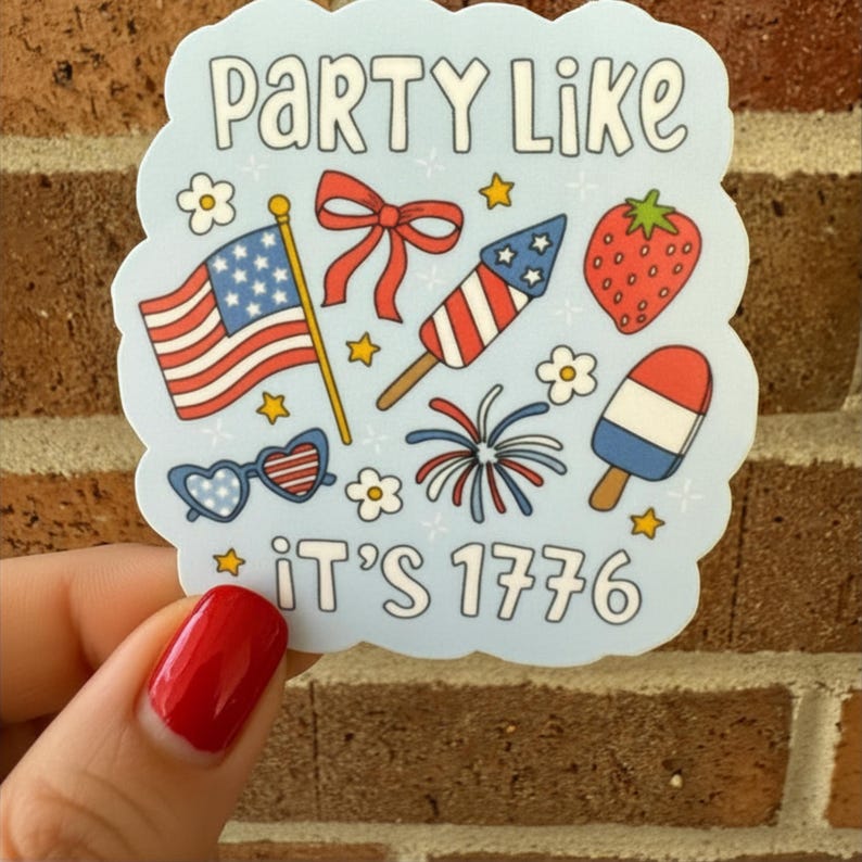 May include: A light blue sticker with the text "Party Like It's 1776". The sticker features illustrations of an American flag, fireworks, a strawberry, and a popsicle. The sticker is held by a hand with red nail polish.
