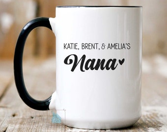 May include: White ceramic mug with a black handle. The mug has black text that reads "KATIE, BRENT, & AMELIA'S Nana" with a small heart symbol.