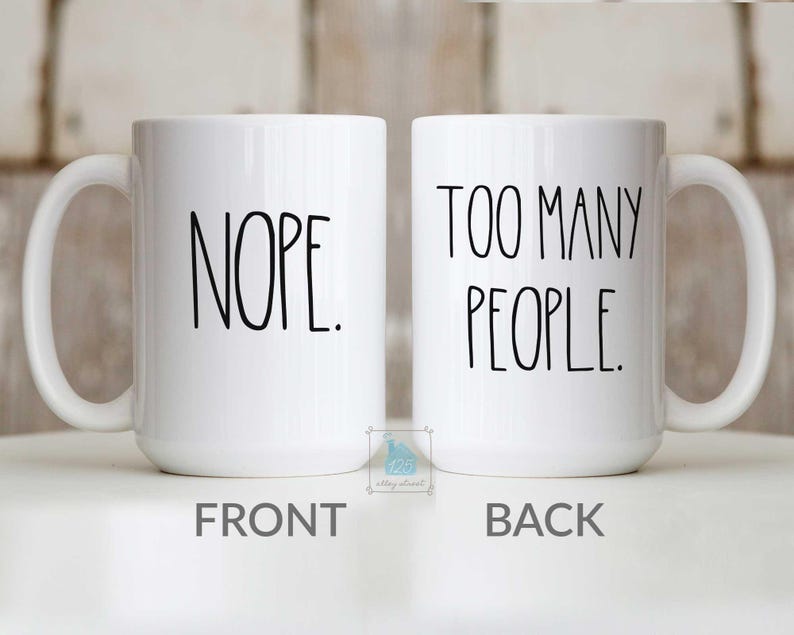 May include: Two white ceramic mugs with black text. One mug reads "NOPE." on the front. The other mug reads "TOO MANY PEOPLE." on the back. Both mugs have a white handle and a simple, modern design.