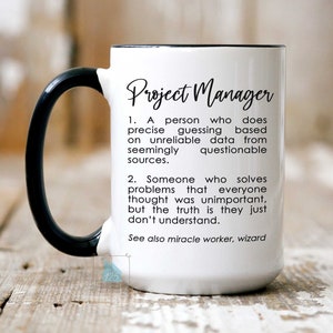 May include: White ceramic mug with a black handle. The mug has a black rim and the text "Project Manager" in black lettering. The text below the title reads: "1. A person who does precise guessing based on unreliable data from seemingly questionable sources. 2. Someone who solves problems that everyone thought was unimportant, but the truth is they just don't understand. See also miracle worker, wizard"