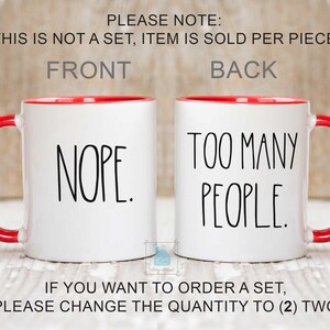 May include: Two white ceramic mugs with red interiors and handles. One mug says "NOPE." in black text, and the other says "TOO MANY PEOPLE." The mugs are displayed side-by-side.