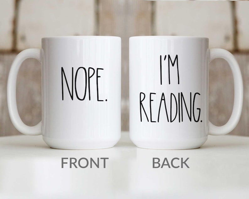 May include: White ceramic coffee mug with black text. The front of the mug says "NOPE." The back of the mug says "I'M READING."