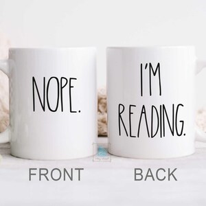 May include: White ceramic coffee mug with black text. The front of the mug says "NOPE." The back of the mug says "I'M READING."