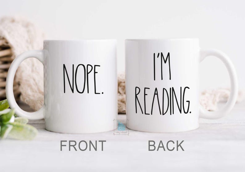 May include: White ceramic coffee mug with black text. The front of the mug says "NOPE." The back of the mug says "I'M READING."