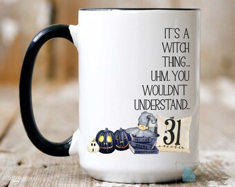May include: White ceramic mug with a black handle. The mug has a black rim and features a Halloween-themed design with the text "It's a witch thing... uhm. You wouldn't understand... 31 october". The design includes a witch's hat, pumpkins, and books with the words "Potions", "Brews", and "Enchantments".