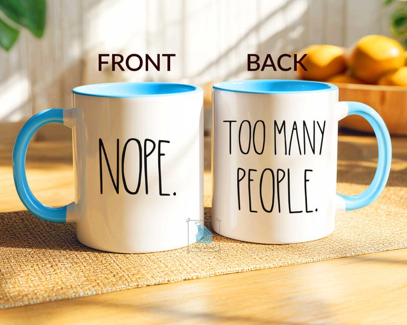 May include: White ceramic mug with a light blue interior, handle, and rim. The front of the mug reads "NOPE." in black text, and the back reads "TOO MANY PEOPLE." A humorous coffee mug.