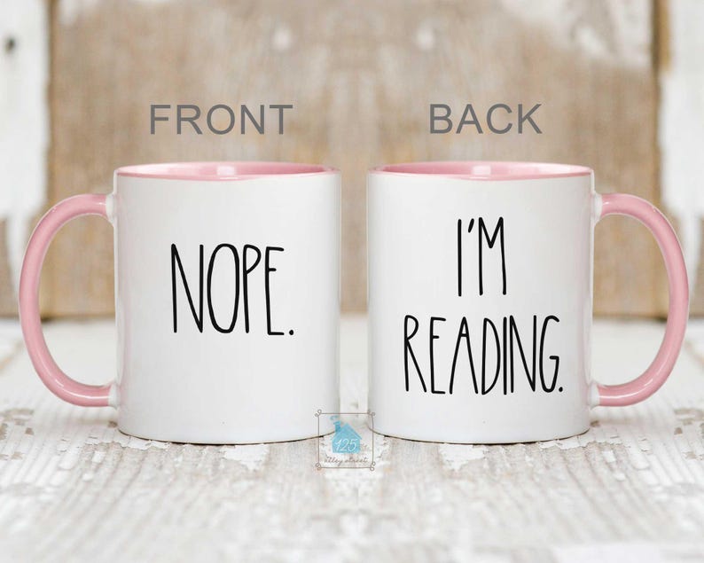 May include: White ceramic coffee mug with a pink rim. The front of the mug says "NOPE." The back of the mug says "I'M READING."